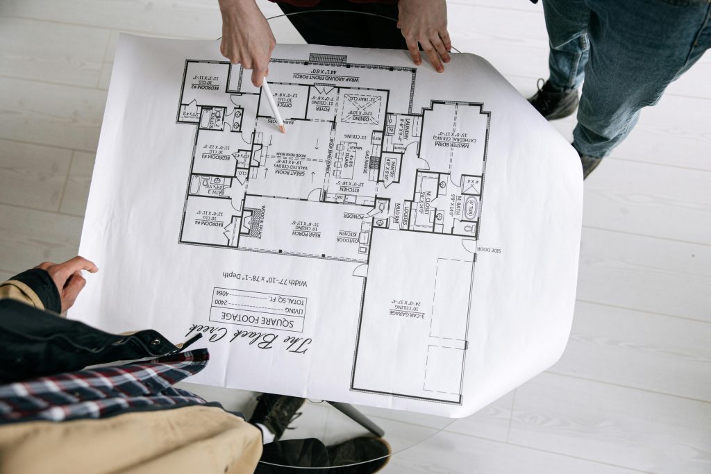 pexels-photo-8962803-8962803 Two architects examining a detailed floor plan blueprint on a table indoors.